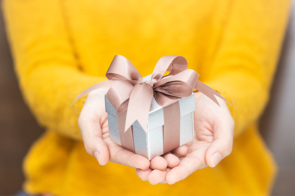 Close-up of hands offering a small silver present wrapped with a pink bow.