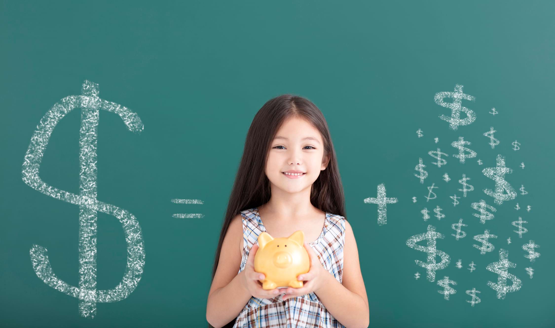 A happy girl holding a piggy bank in front of a blackboard