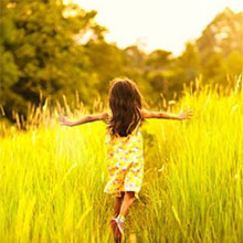 A young girl running into a sunlit field of tall grass.