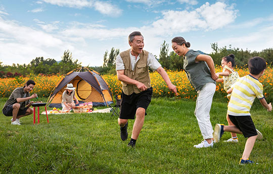 A multi-generational Asian family happily playing and barbecuing at an outdoor grassy campsite