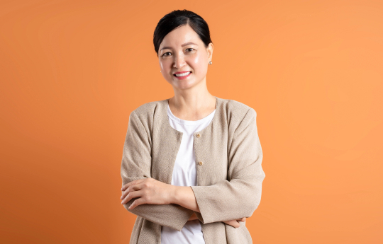 A smiling middle-aged Asian woman posing with crossed arms
